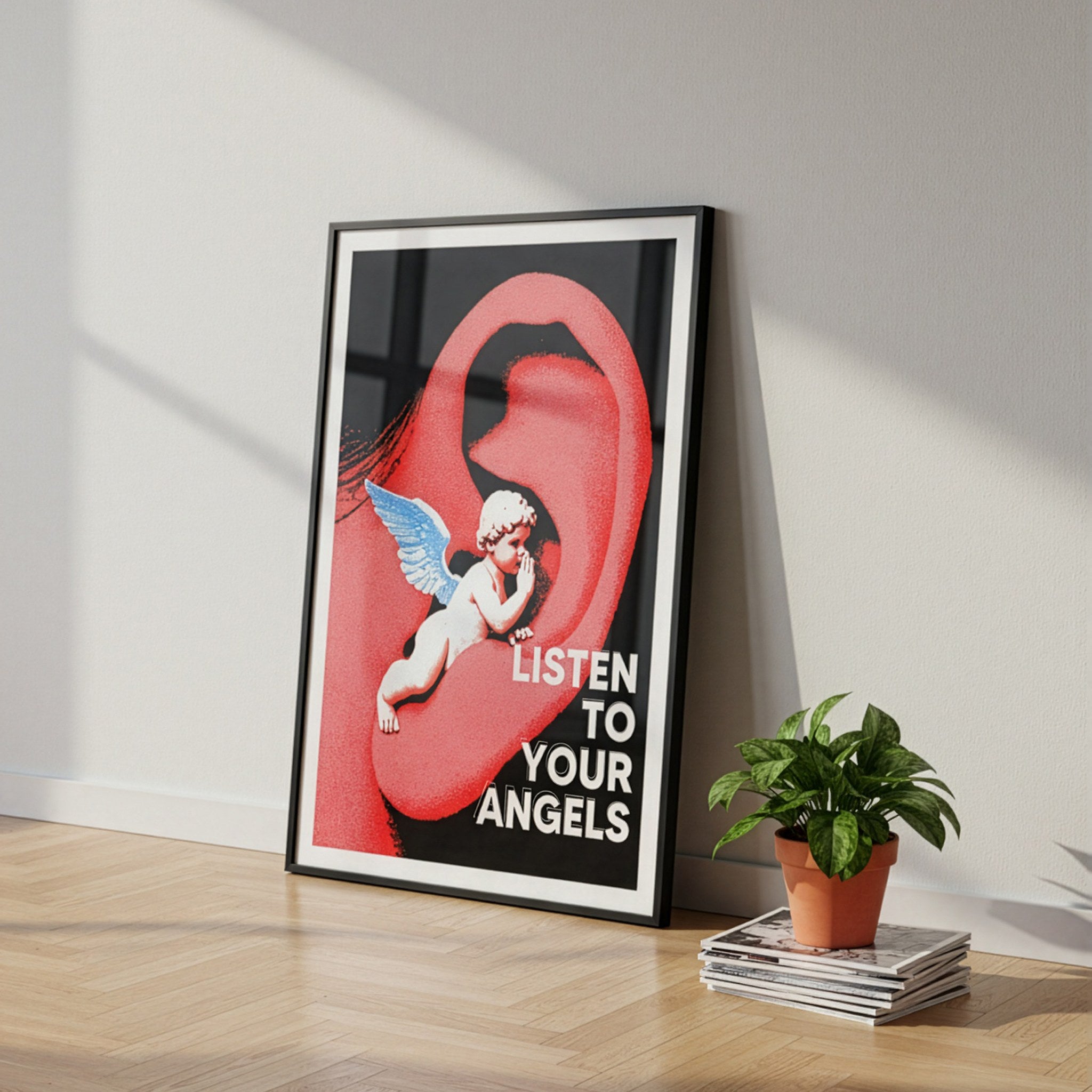 Melek ve kulak temalı pop art poster, ahşap zeminde siyah çerçeveyle duvara yaslanmış